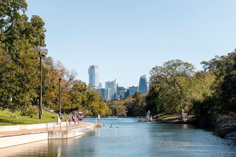 A sunny day at Barton Springs Pool with the Austin skyline in the background