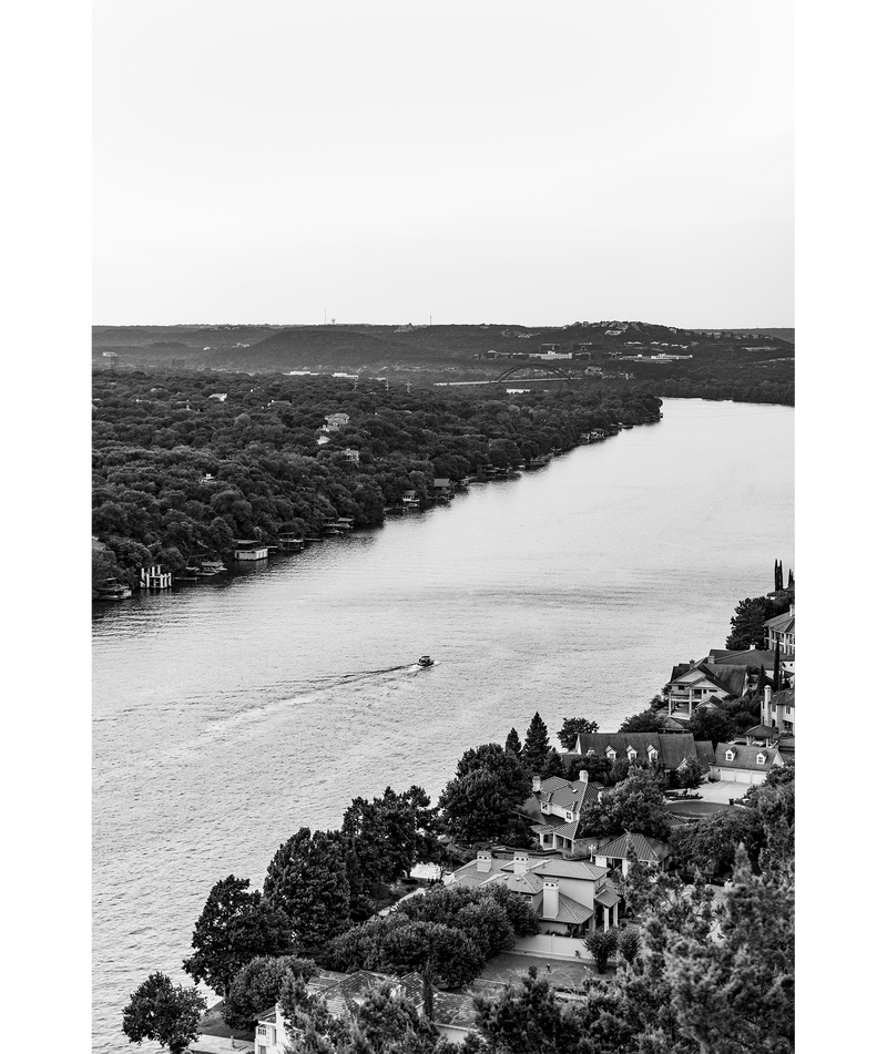 A black and white image of a boat traveling along Lake Austin as seen from Mount Bonnell