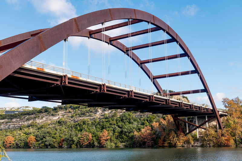 The Pennybacker Bridge against a blue sky and surrounded by fall foliage